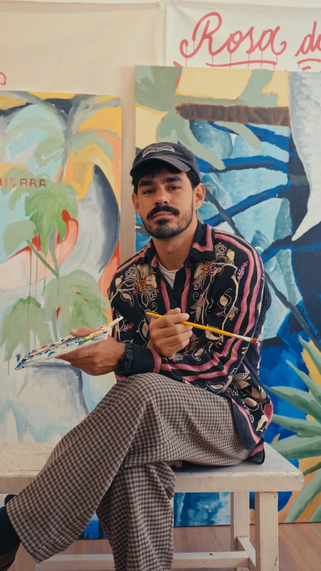 Diguila, artista plástico, sentado em frente às suas telas