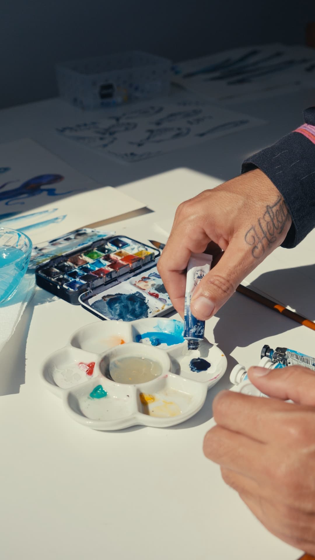 Mãos a misturar tinta azul numa paleta de porcelana